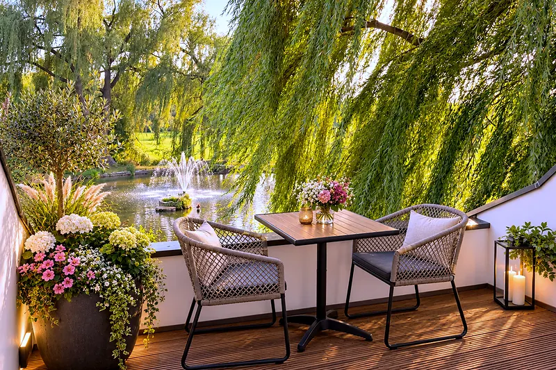 Terras van de suite Schwarzer Schwan aan het water, een tafel voor twee onder de treurwilg